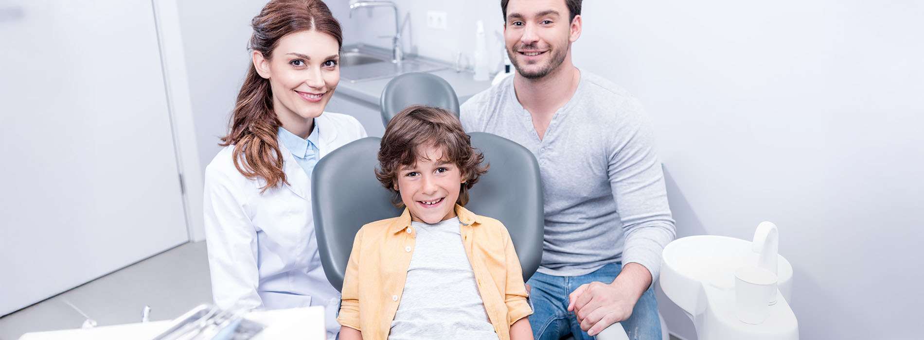 The image features a family sitting in a dental chair with a dentist, capturing a moment during their visit to the dentist.