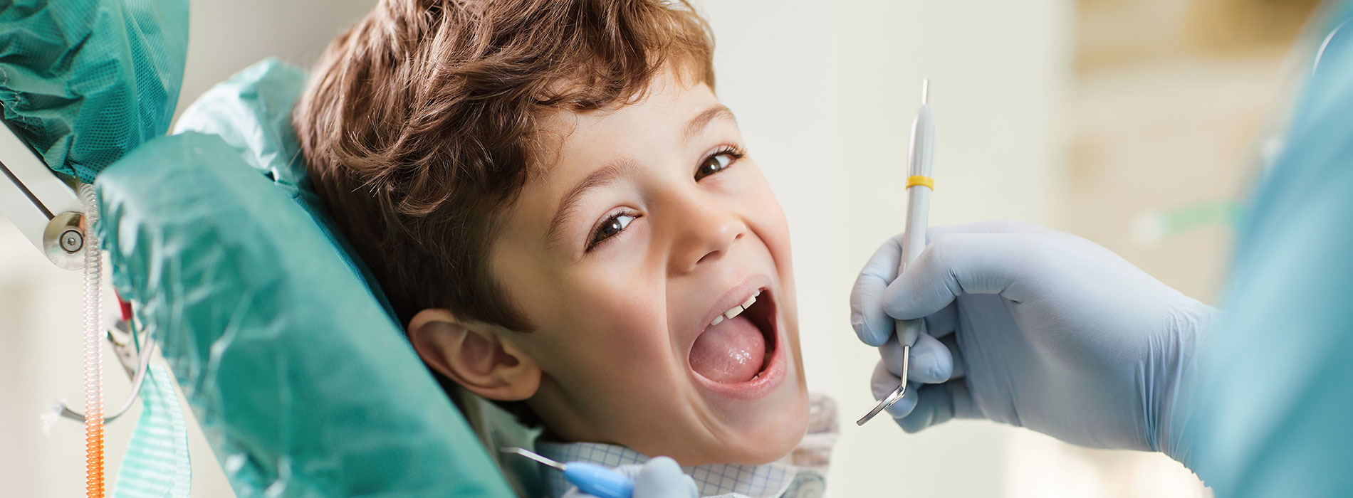 A young child receiving dental treatment with a dentist s hand holding a syringe over their mouth.