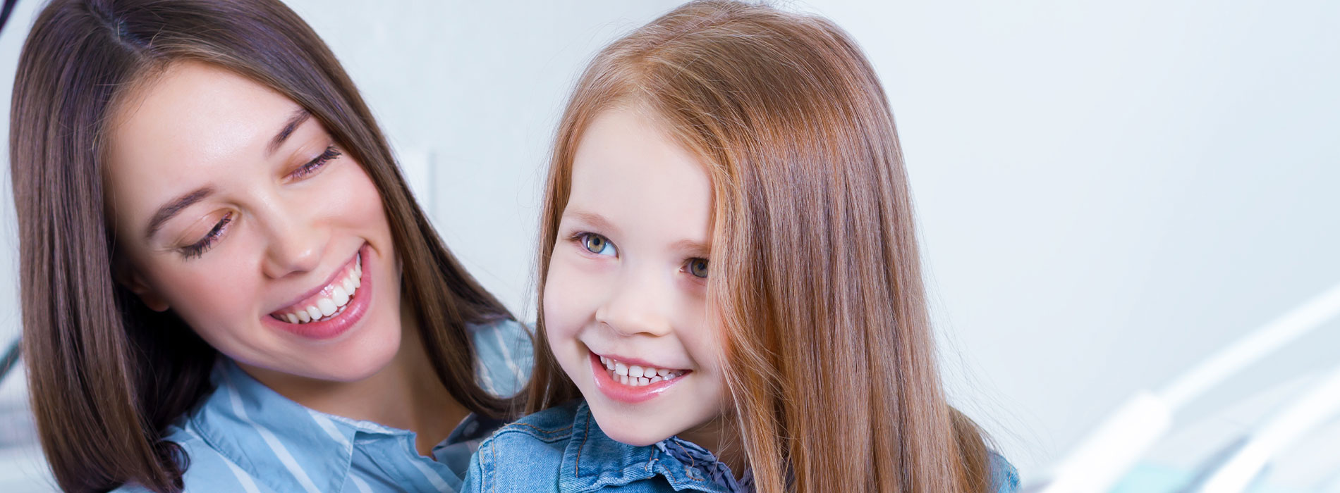 The image shows a woman and a young girl smiling at the camera, with the woman s arm wrapped around the child. They are standing indoors with a blurred background that suggests a domestic setting.