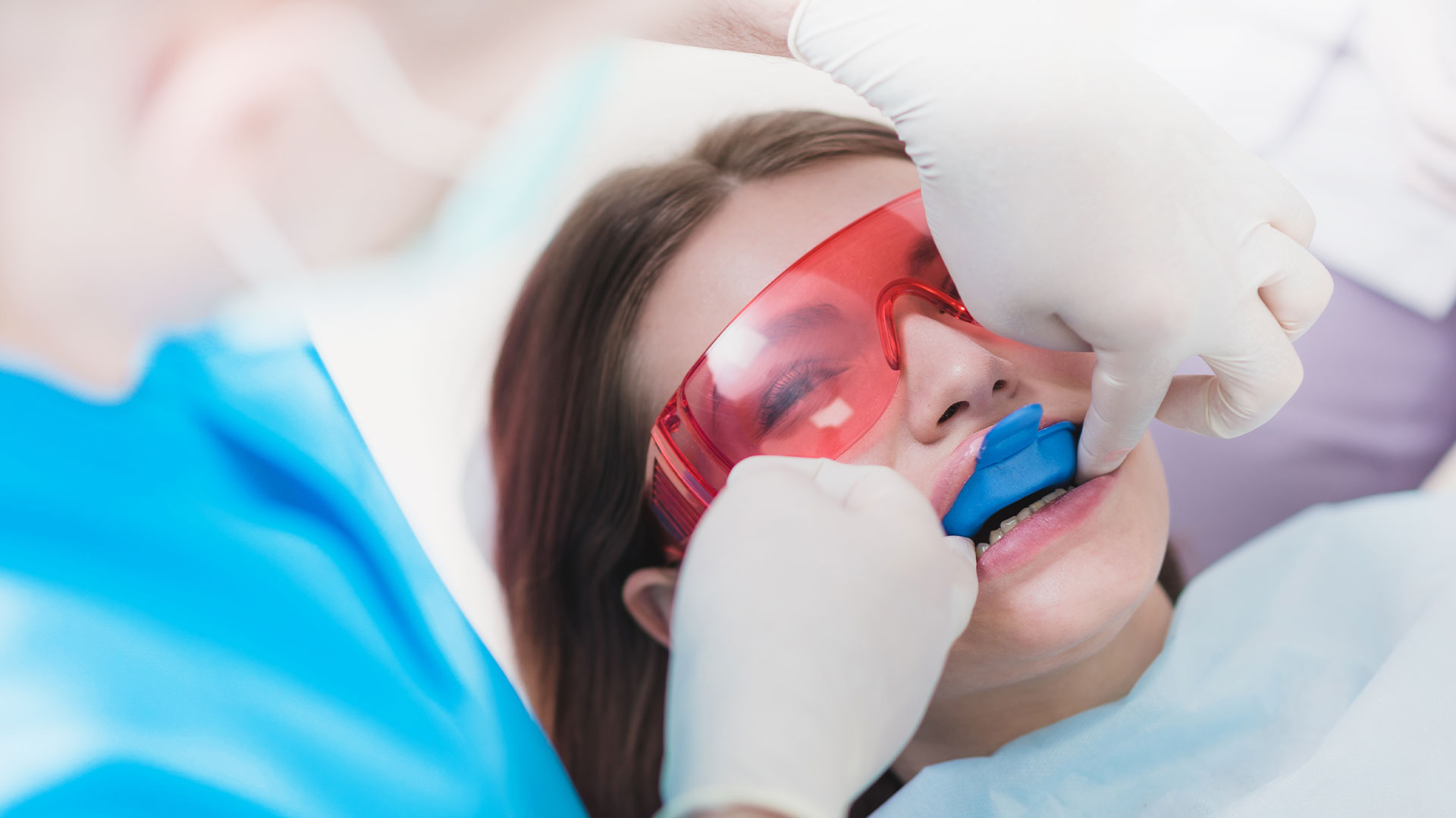 Woman undergoing dental procedure with red goggles on her eyes, being attended to by medical professionals.