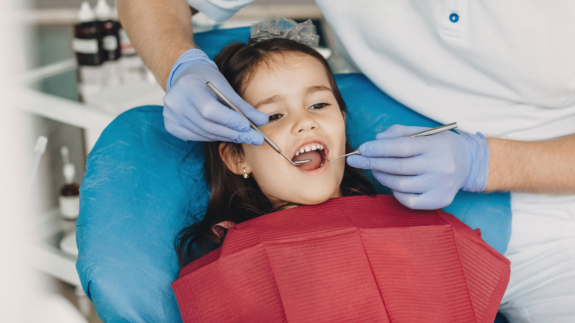 A young child sitting on a dental chair receiving dental treatment with a dentist performing the procedure.