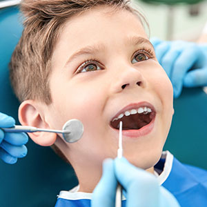 A young boy sitting in a dental chair with his mouth open, receiving dental care from a professional.