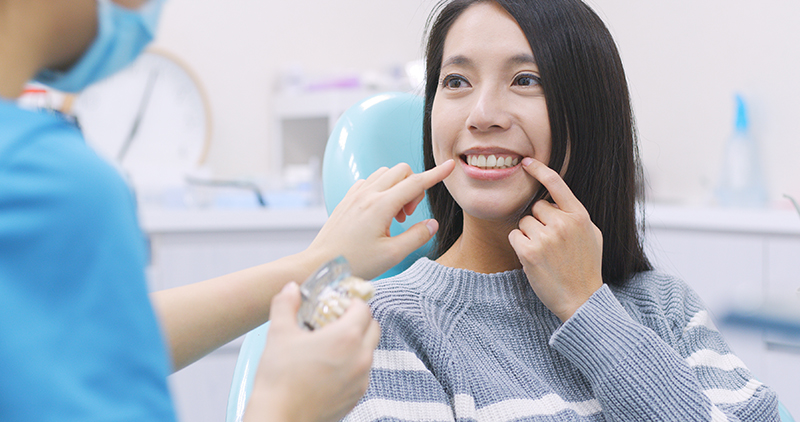 A young woman with straight teeth receiving dental care while sitting in a dentist s chair, with a dental professional assisting her.