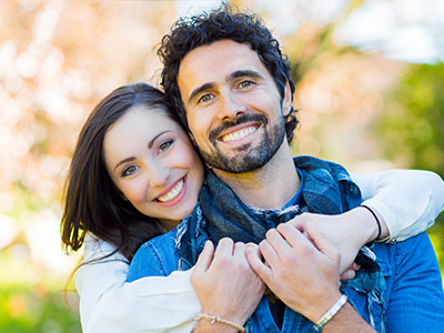 A man and woman hugging each other outdoors, smiling and seemingly happy.