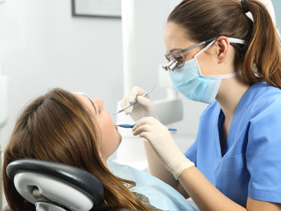 Woman wearing a surgical mask adjusting woman s teeth in dental chair.