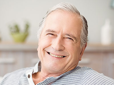The image shows an older man with a smile on his face, leaning back in a chair, seemingly relaxed and content.
