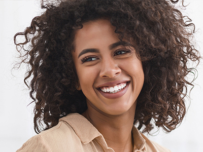 The image shows a smiling woman with curly hair, wearing a beige top, against a white background.